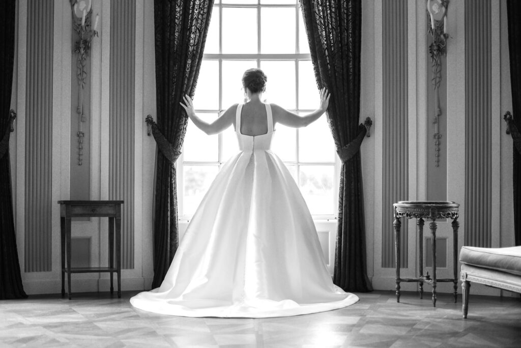 Prachtige bruid met mooie witte jurk staat voor een groot raam gefotografeerd door trouwfotograaf Novo Fotografie in een trouwlocatie in Deventer